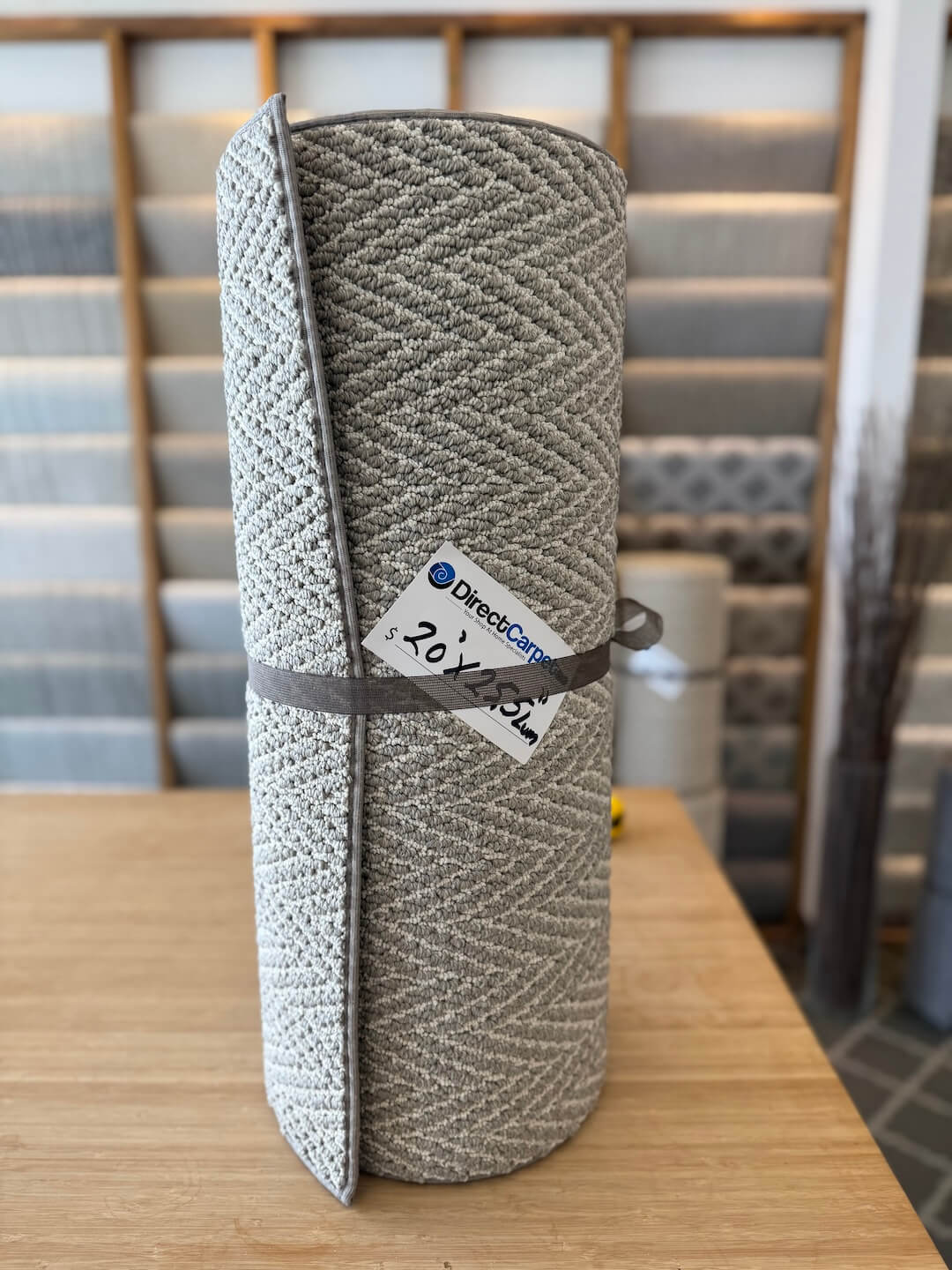 Rolled-up carpet with a brand label on a wooden table, with carpet samples in the background.