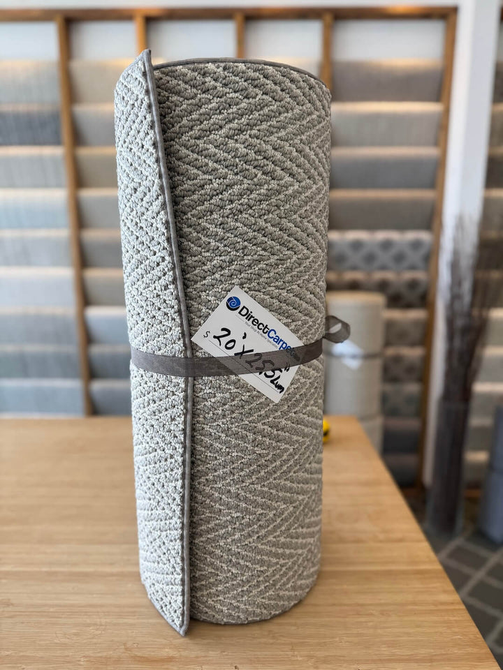 Rolled-up carpet with a brand label on a wooden table, with carpet samples in the background.