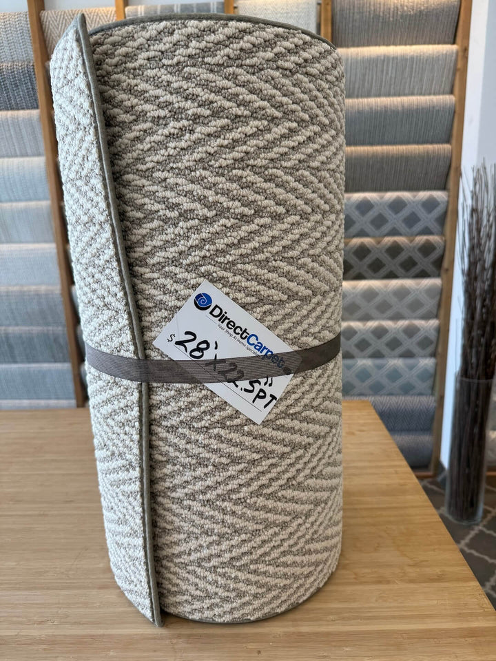 Rolled-up textured rug with a price tag on a wooden surface, with carpet samples in the background.