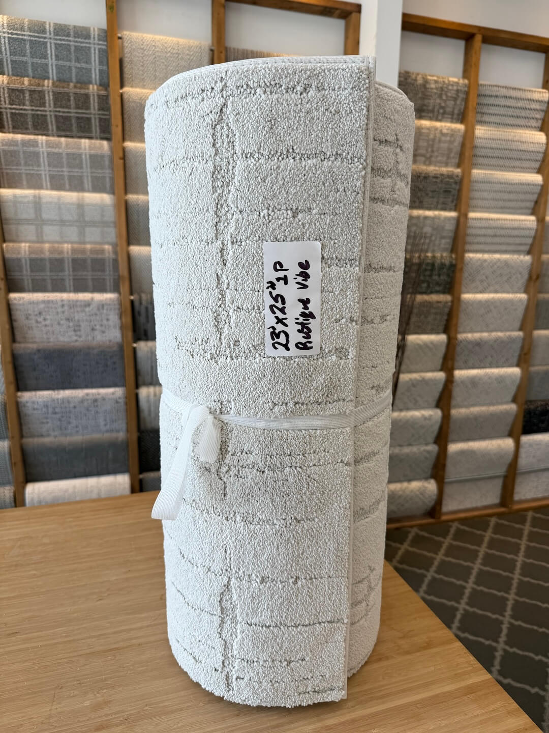 Roll of textured white fabric on a wooden table with a blurred background of more fabric rolls.